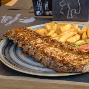 Costine di maiale glassate con salsa barbecue servite con patatine rustiche, lattuga e pomodoro nel piatto del ristorante