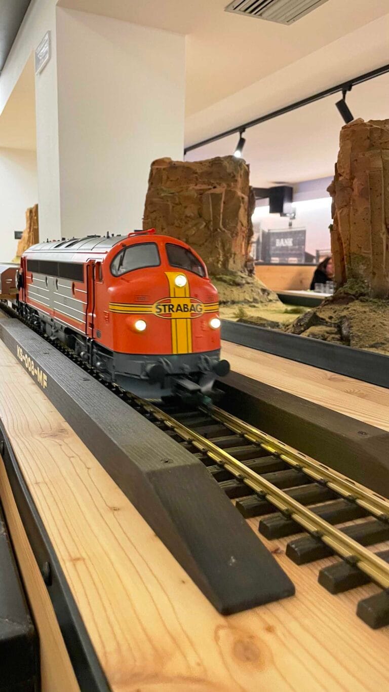 Red STRABAG locomotive model moving on wooden tracks inside the restaurant