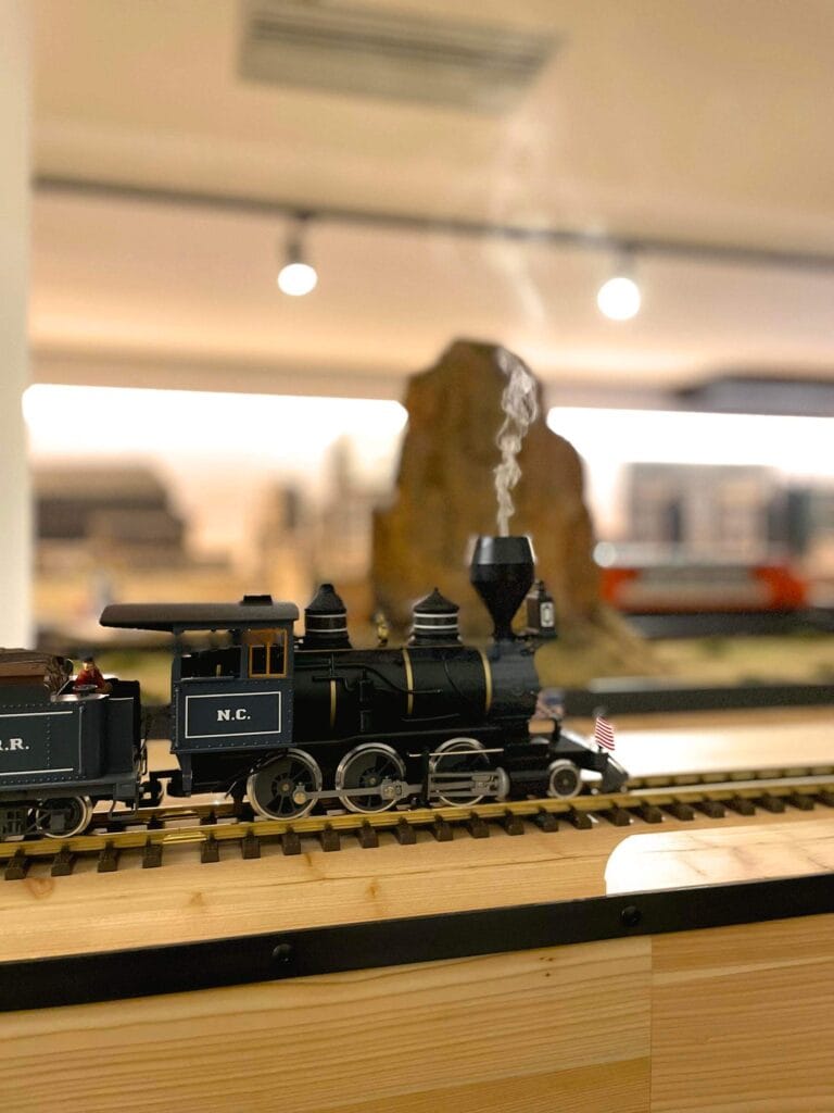 Modellino di locomotiva a vapore N.C. in movimento su binario in legno, con fumo realistico e bandiera americana